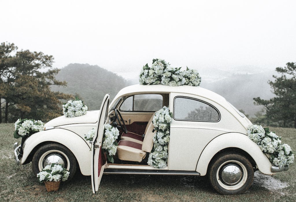 A vintage car adorned with flowers, parked in a misty rural field, capturing a romantic wedding vibe.