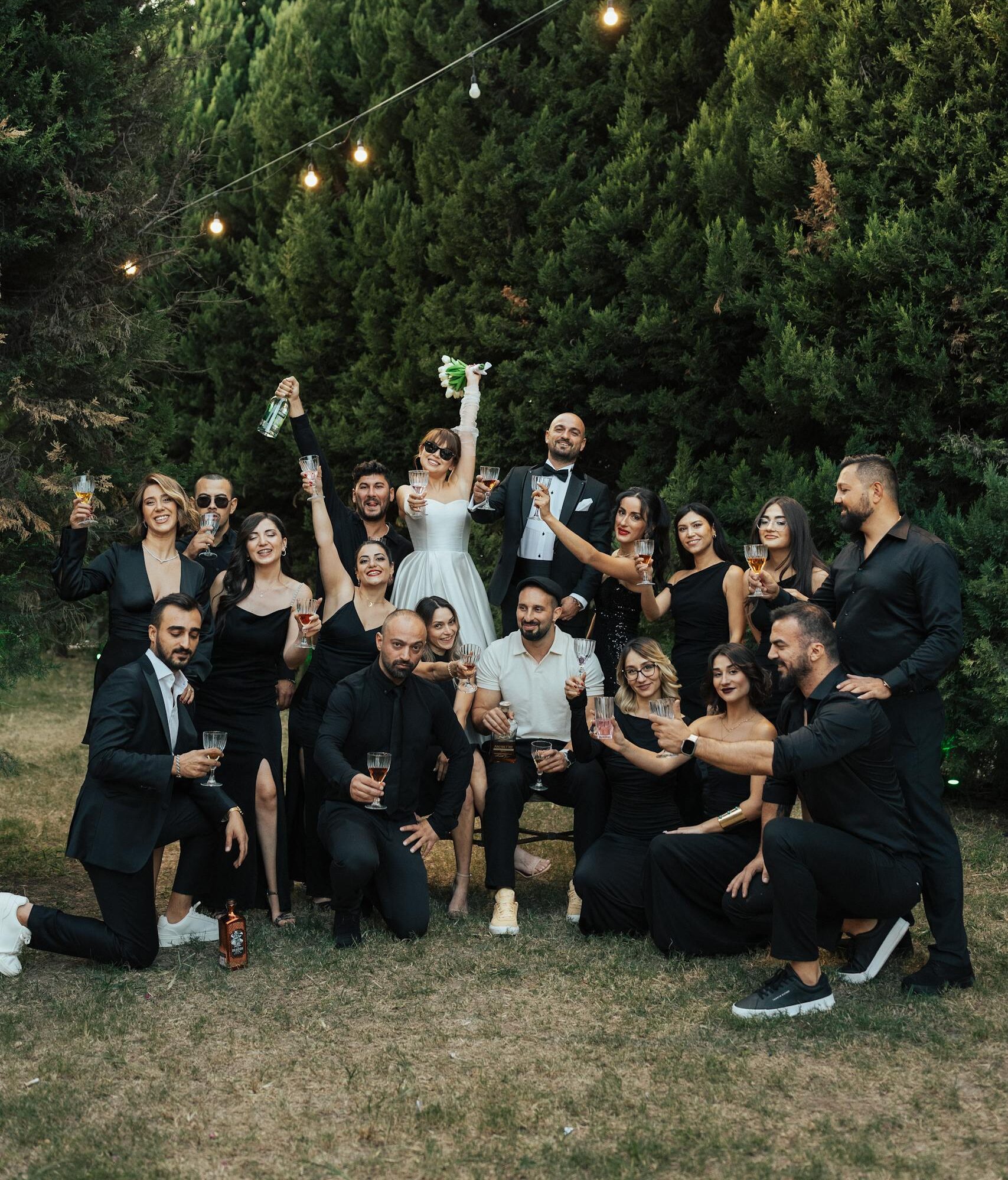 A joyful group celebrating a wedding outdoors under string lights.